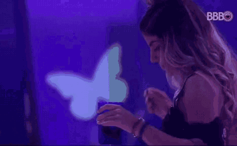 a woman is drinking from a blue cup in front of a butterfly projection on the wall .