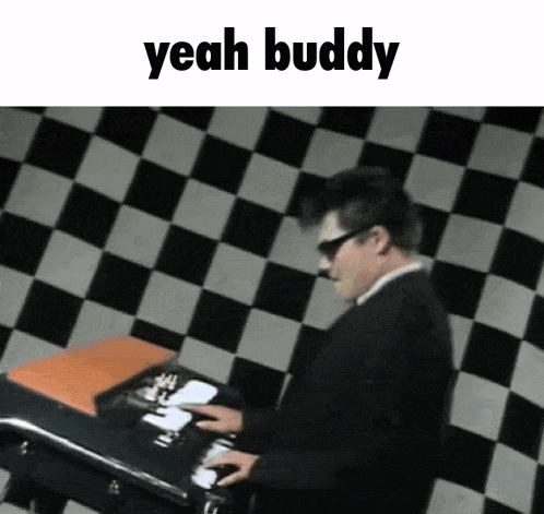 a man in a suit and sunglasses is playing a keyboard with the words yeah buddy above him