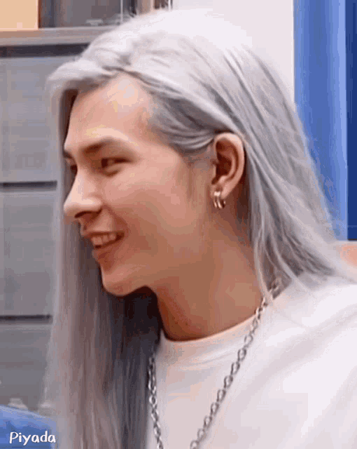 a man with long white hair and earrings is smiling