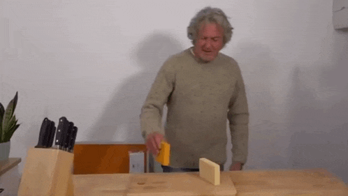 an older man is cutting a piece of cheese on a wooden cutting board .