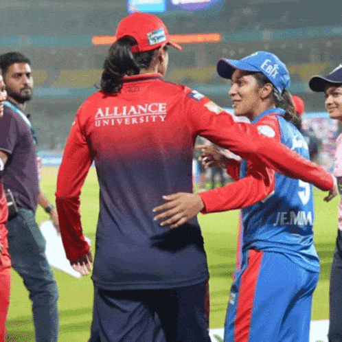 a woman wearing a red alliance university jersey is hugging another woman