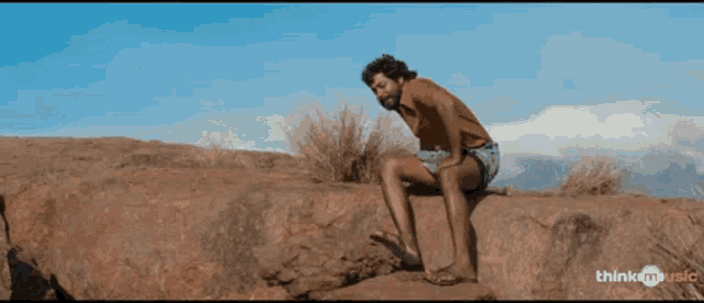 a man squatting on a rock with a think music logo in the background