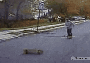 a person is riding a skateboard down a street with a gifbin.com logo in the corner