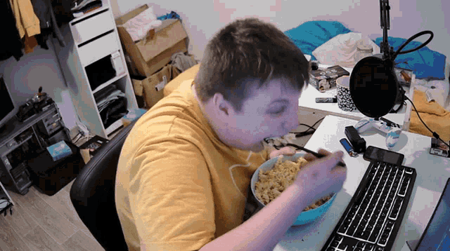 a man in a yellow shirt is eating macaroni and cheese from a bowl