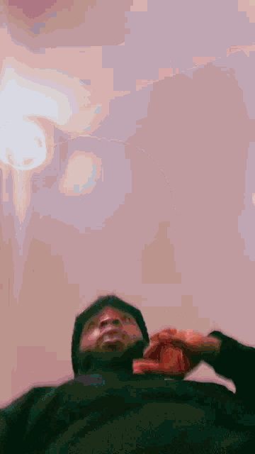 a man in a black hoodie is laying on a bed looking up at the camera