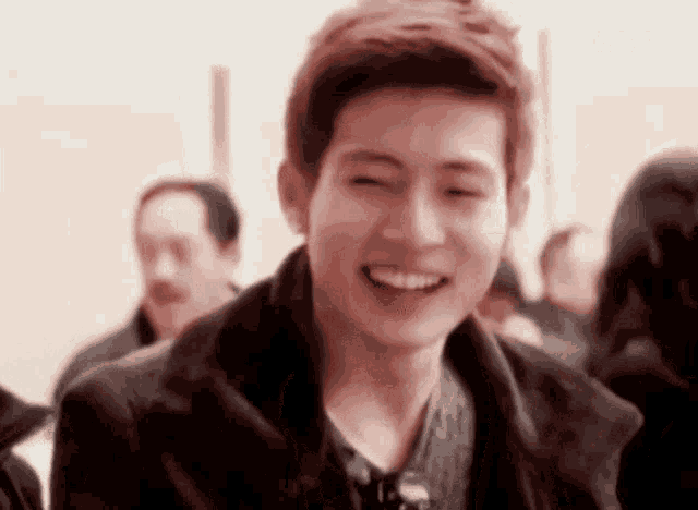 a young man is smiling with his eyes closed in a crowded room .