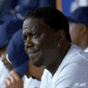 a man in a baseball uniform is sitting in a dugout with other baseball players .