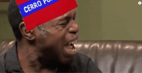 a man sitting on a couch with a red and blue sign over his head that says cerro