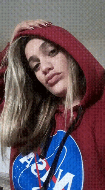 a woman wearing a red nasa hoodie holds her hand to her head