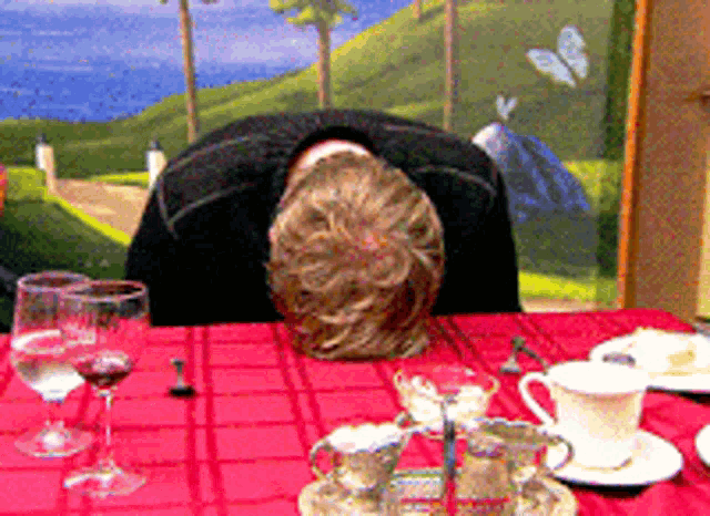 a person laying their head on a table with a painting in the background