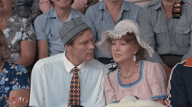 a man and a woman are sitting next to each other in a crowd with the word " a2mo " in the corner
