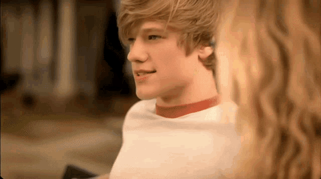 a blonde boy wearing a white shirt and a red collar looks at a blonde woman