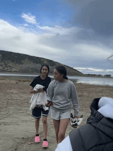 two girls walking on a beach with one wearing a sweatshirt that says ' adidas '