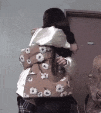 a woman in a floral jacket is hugging another woman in a brown jacket