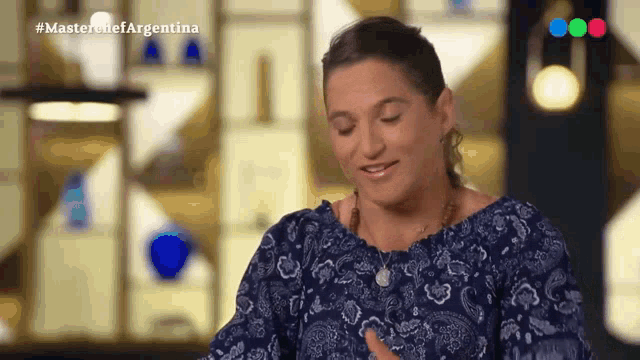 a woman in a blue paisley top is sitting in front of a screen that says masterchef argentina on it