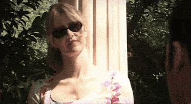 a woman wearing sunglasses stands in front of a pillar