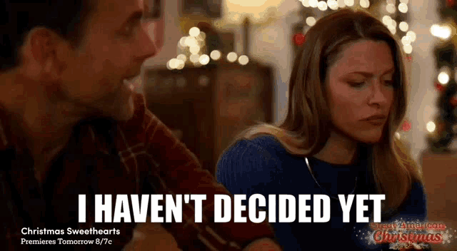 a man and a woman are sitting in front of a christmas tree and the woman says i haven 't decided yet .