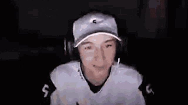 a young man wearing headphones and a hat is sitting in front of a computer screen .