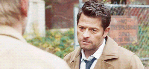 a man in a trench coat and tie is talking to another man in a park .