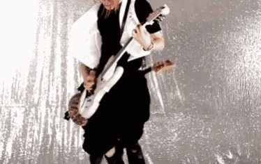a man is playing a white electric guitar in front of a silver background .