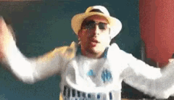 a man wearing a hat and sunglasses is dancing with his arms in the air .