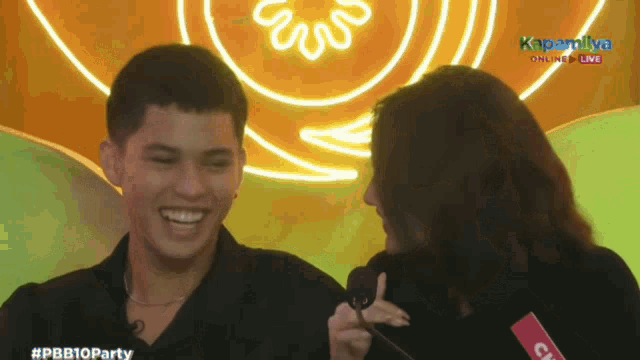 a man and a woman are laughing in front of a sign that says kapandiya online live