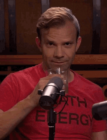 a man in a red death energy shirt is holding a glass in front of a microphone