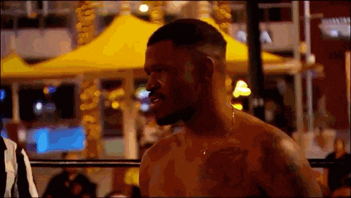 a man without a shirt is standing in a boxing ring with a yellow tent in the background .