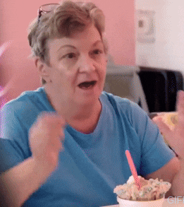a woman in a blue shirt is sitting at a table eating ice cream