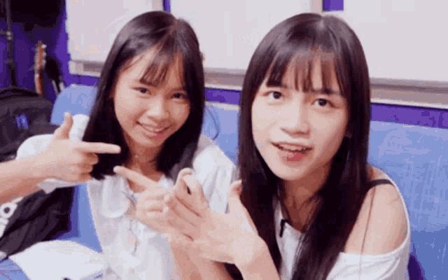 two girls are sitting next to each other on a blue couch and one is pointing at the other .
