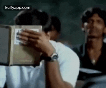 a man is covering his face with a book while another man looks on .