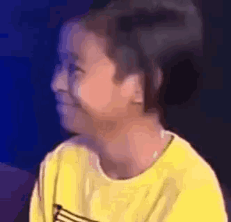a young girl in a yellow shirt is smiling and looking at the camera .