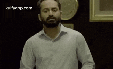 a man with a beard wearing a white shirt is standing in front of a wall .