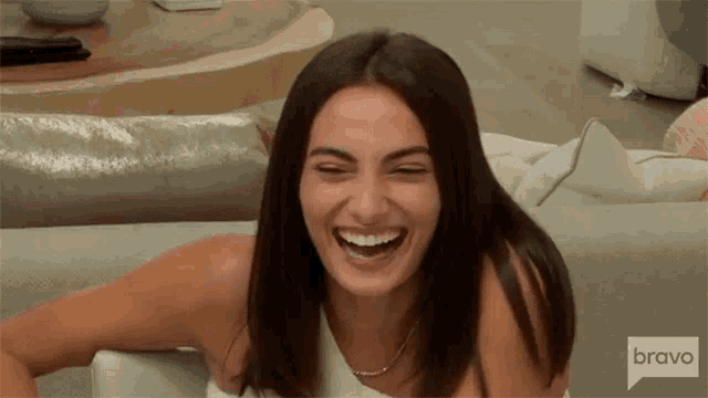 a woman is laughing while sitting on a couch on bravo television .