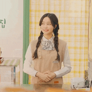a woman wearing an apron and a plaid bow tie stands in front of a checkered curtain