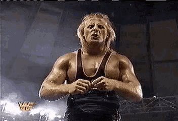 a wrestler in a black tank top is standing in a stadium .
