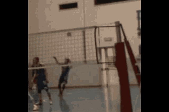 two people are playing volleyball in a gym .