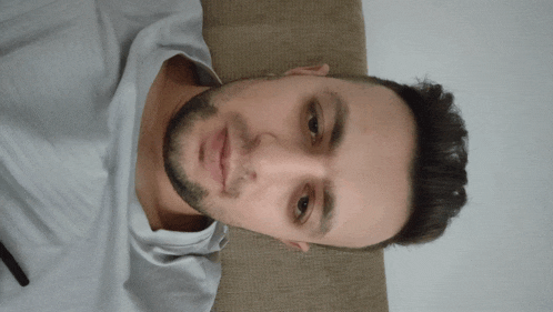 a man with a beard and a white shirt looks down at the camera