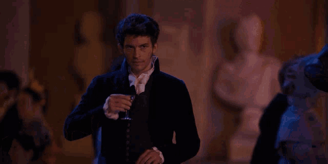 a man in a black suit drinks from a glass