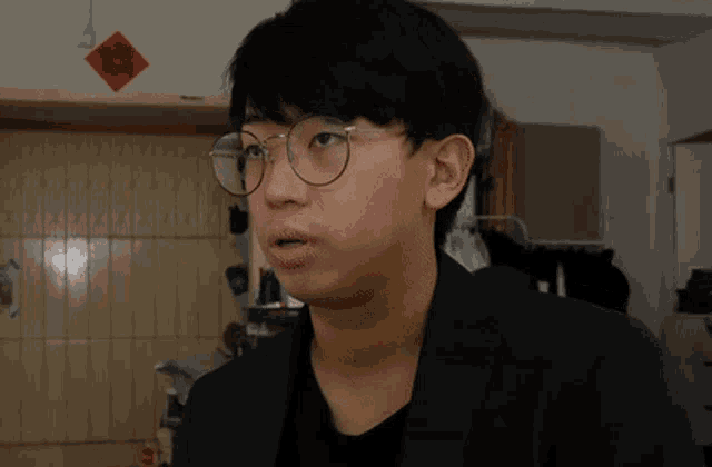 a young man wearing glasses and a black jacket looks surprised