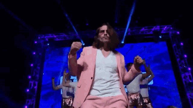 a man in a pink suit and white shirt is dancing on a stage