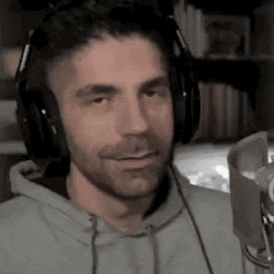 a man wearing headphones and a hoodie is talking into a microphone .