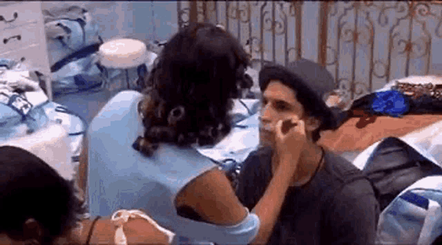 a woman is applying makeup to a man 's face while wearing a hat .