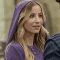a woman in a purple dress and purple head scarf is talking to a man .