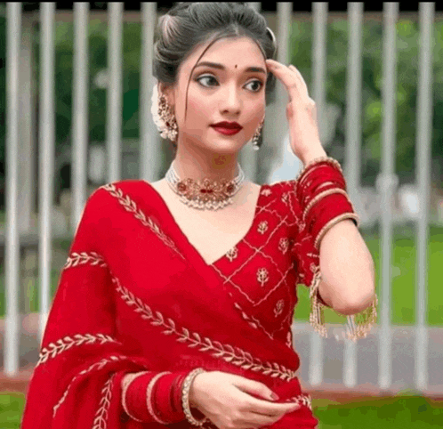 a woman is wearing a red saree with gold embroidery and a necklace .