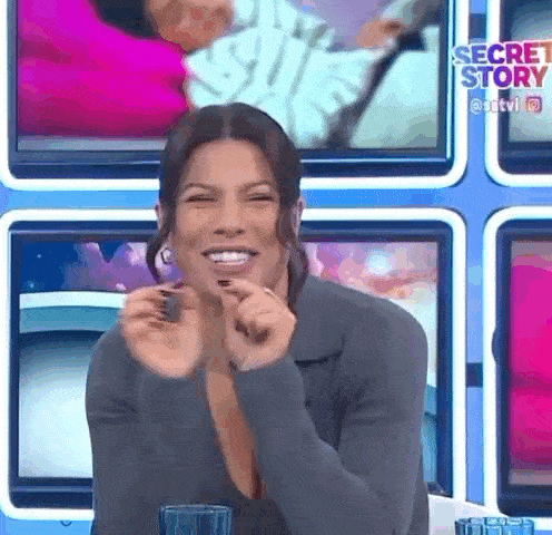 a woman is sitting at a table with a glass of water in front of a screen that says secret story .