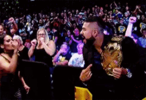 a man holding a wrestling championship stands in front of a crowd of people