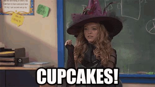 a girl in a witch costume is standing in front of a blackboard and says cupcakes !