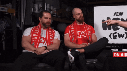 two men sitting in front of a sign that says aew