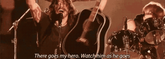 a man is singing into a microphone while holding a guitar in front of a drum set .
